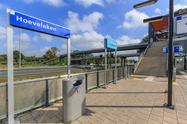 Station Hoevelaken met perron, trappen en bewegwijzering op een zonnige dag.